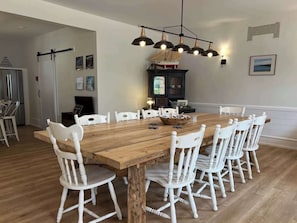 Ein Esszimmer mit Holztisch und weißen Stühlen, einem dunklen Schrank und einer hängenden Leuchte.