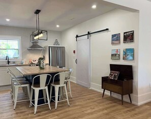 A modern kitchen with a wooden table, white chairs, a stainless steel refrigerator, and a sliding door.