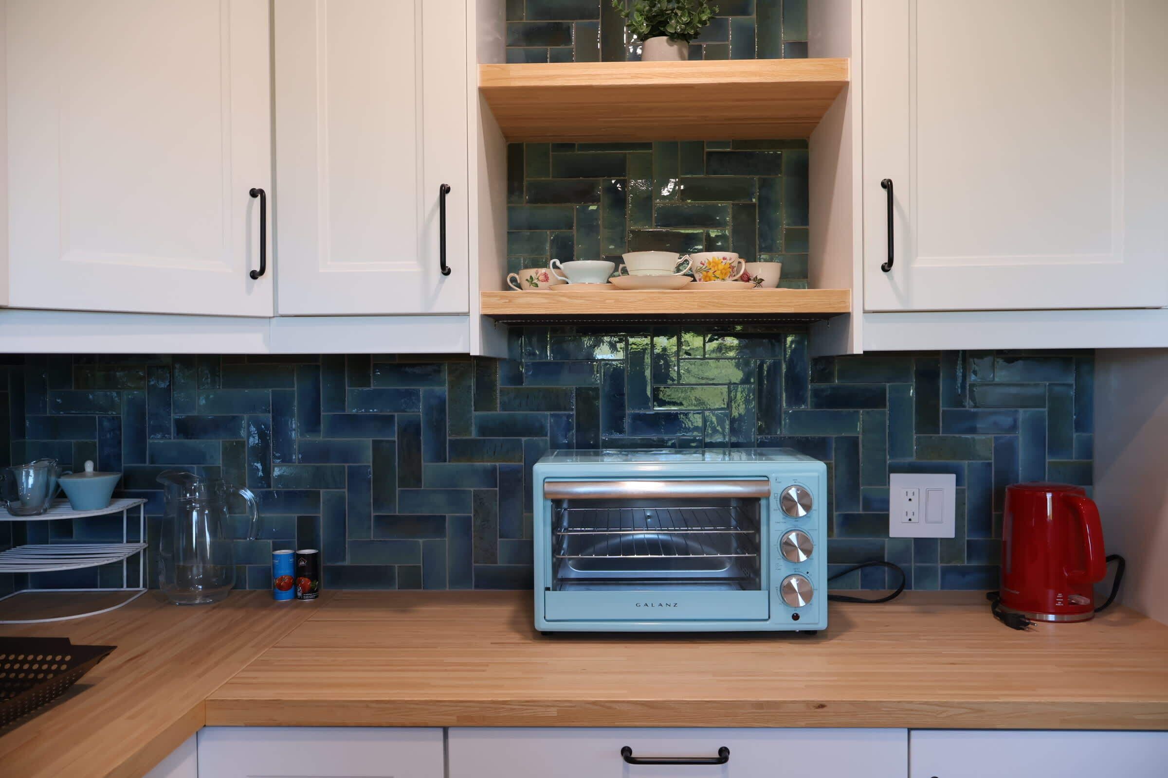Eine Küche mit weißen Schränken, einem blauen Toaster, einer roten Kaffeemaschine und einem Regal mit Tassen und einer Kanne.