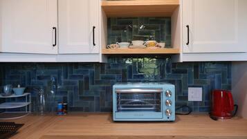 Eine Küche mit weißen Schränken, einem blauen Toaster, einer roten Kaffeemaschine und einem Regal mit Tassen und einer Kanne.