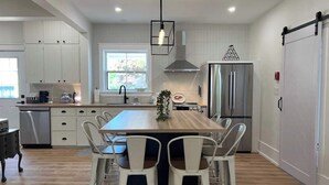 A modern kitchen with white cabinetry, a central island, stainless steel appliances, and a dining area with white chairs.