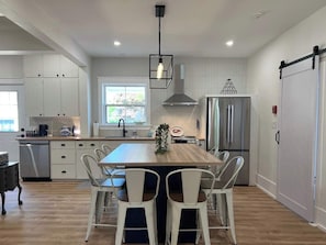A modern kitchen with white cabinetry, a central island, stainless steel appliances, and a dining area with white chairs.