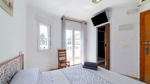 Un dormitorio con cama, una silla, un escritorio, un armario y un ventanal corredero al exterior.