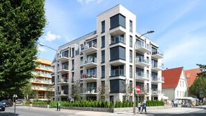 Un immeuble moderne à plusieurs étages, doté de balcons, donnant sur la rue et offrant une vue sur un ciel dégagé.