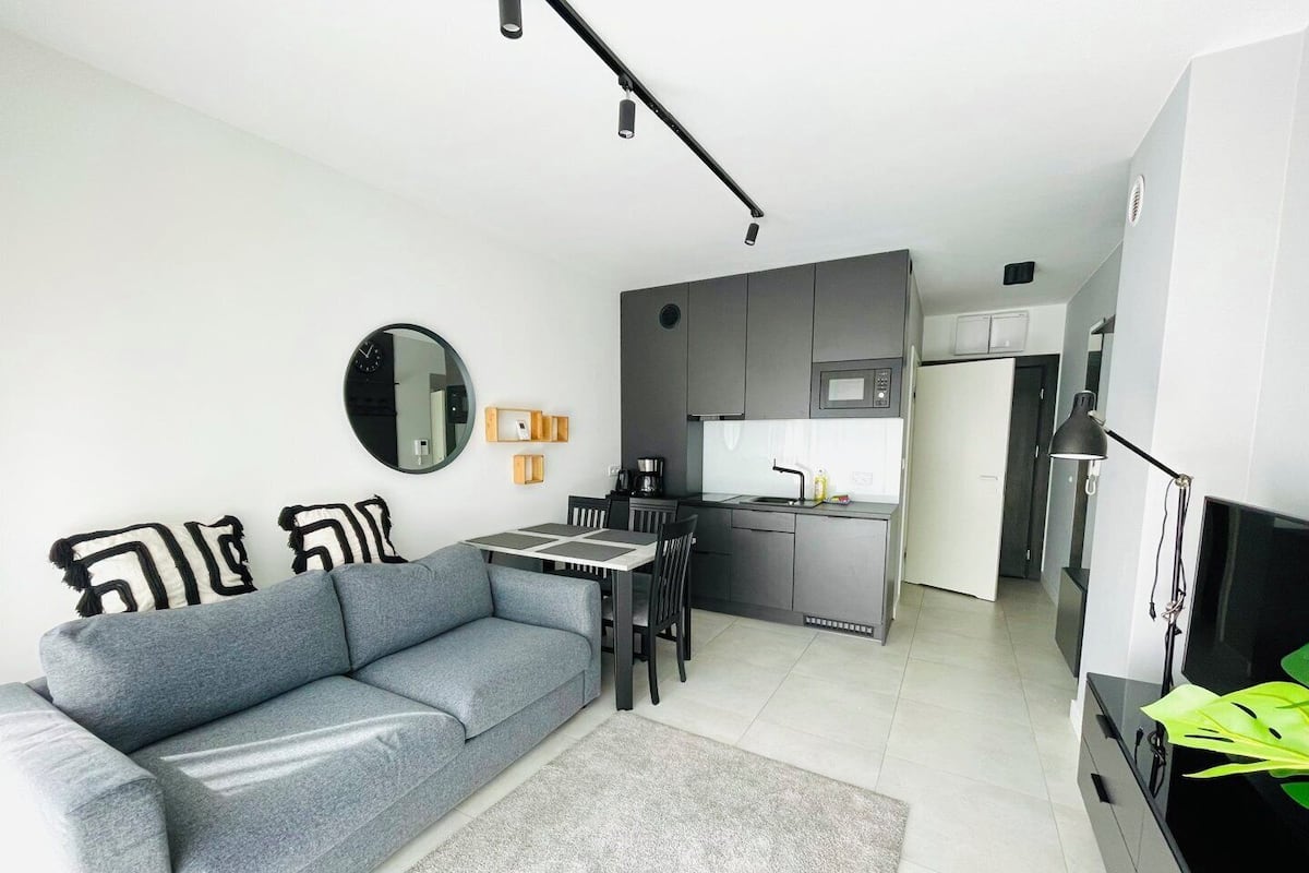 A modern living room with a grey sofa, a round mirror, and a small dining table.