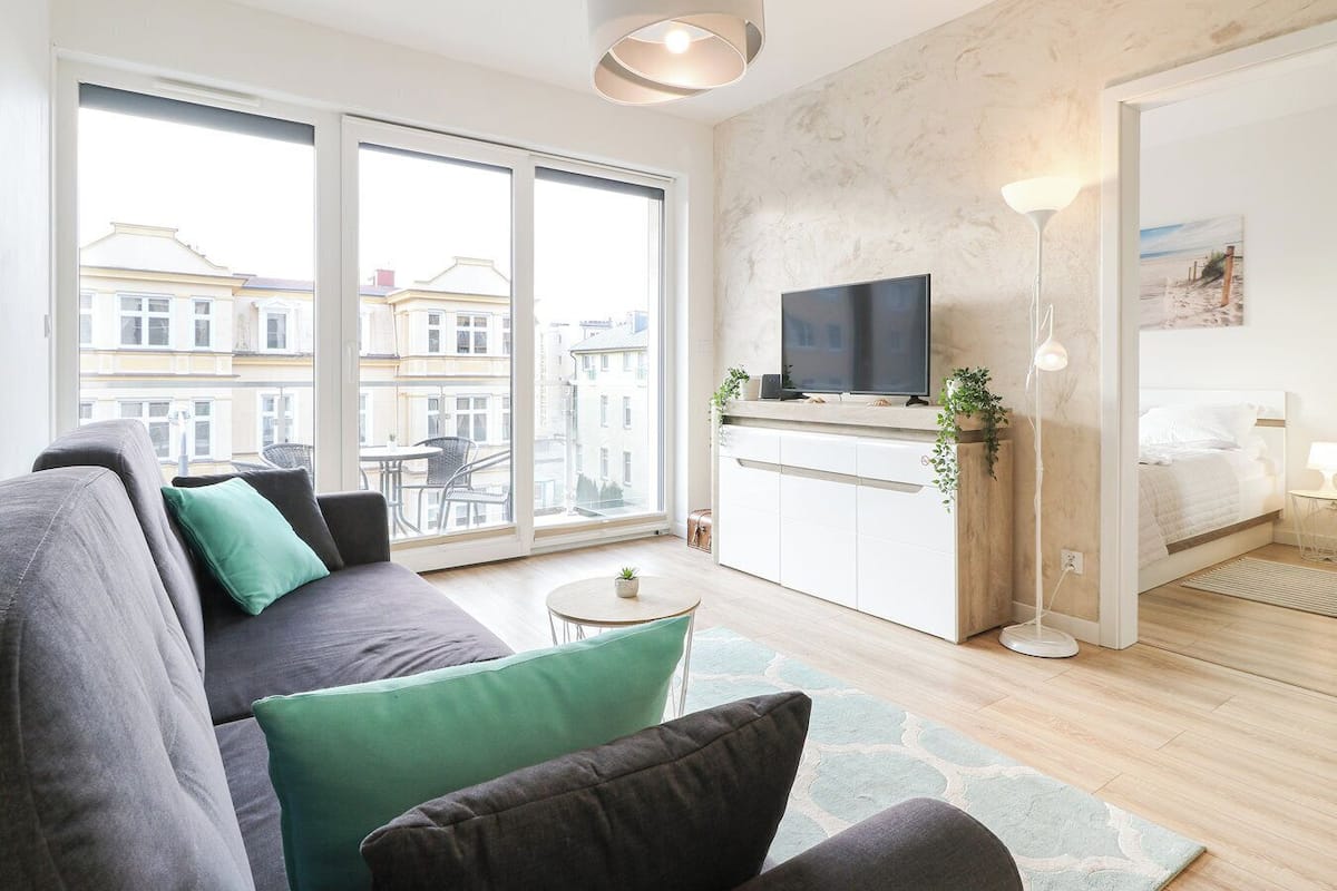 A modern apartment with a large window, a sofa, a TV, and a small table.