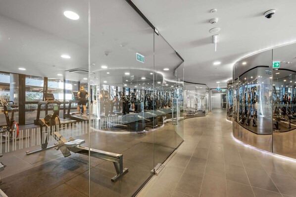 Un gimnasio moderno con paredes de vidrio, varios equipos de ejercicio y un interior limpio y bien iluminado.