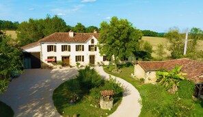A two-story house with a tiled roof, surrounded by greenery and a gravel driveway. - Charming residence "Au Coeur de la Gascogne".  Gîte sleeps 7. (Montesquiou)