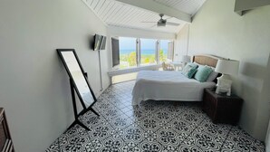 Un dormitorio con cama, escritorio, silla, televisión y vista al océano.