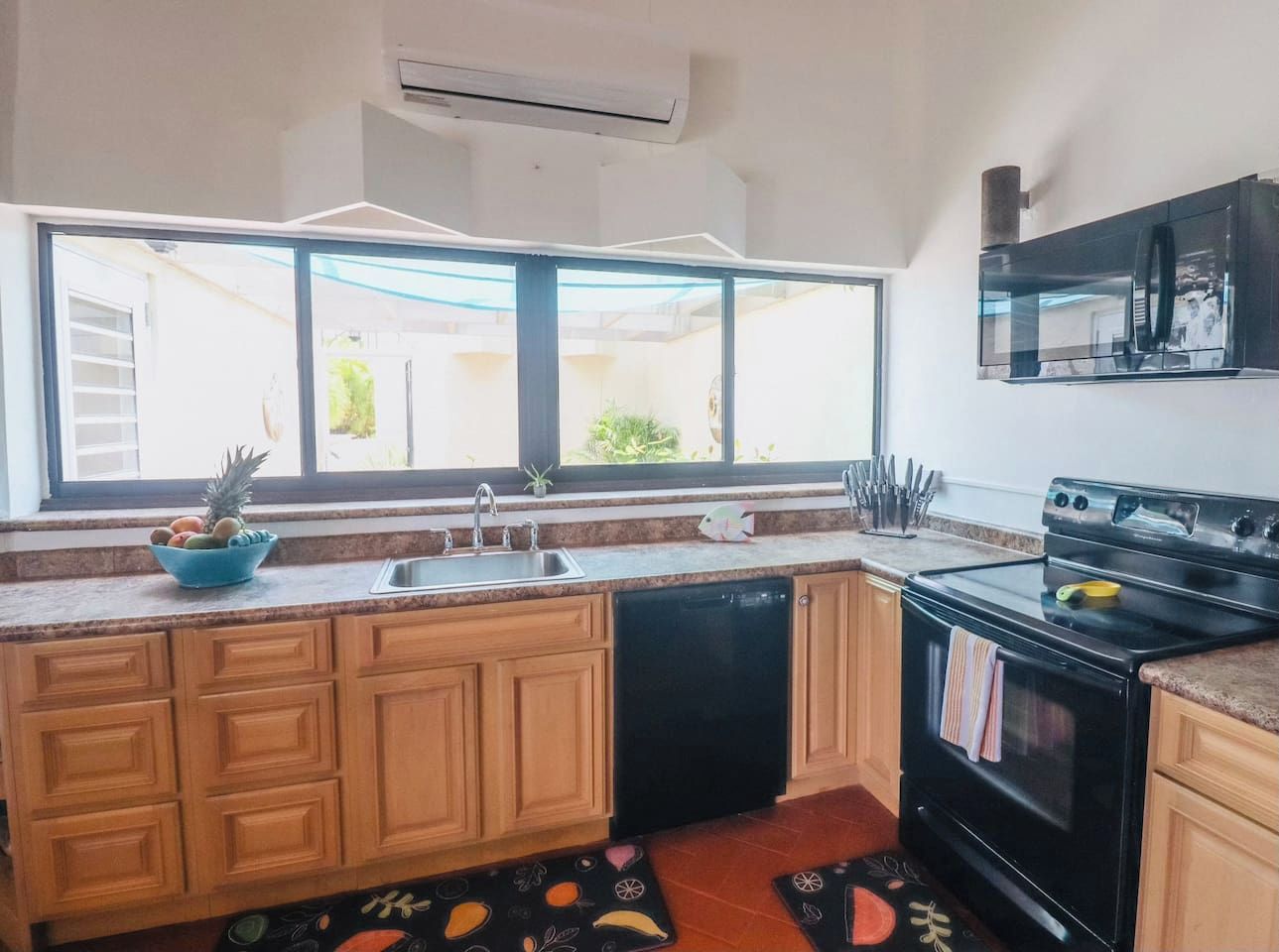 Cocina con gabinetes de madera, lavavajillas negro, estufa y ventana con vistas al exterior.