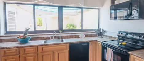 Cocina con gabinetes de madera, lavavajillas negro, estufa y ventana con vistas al exterior.