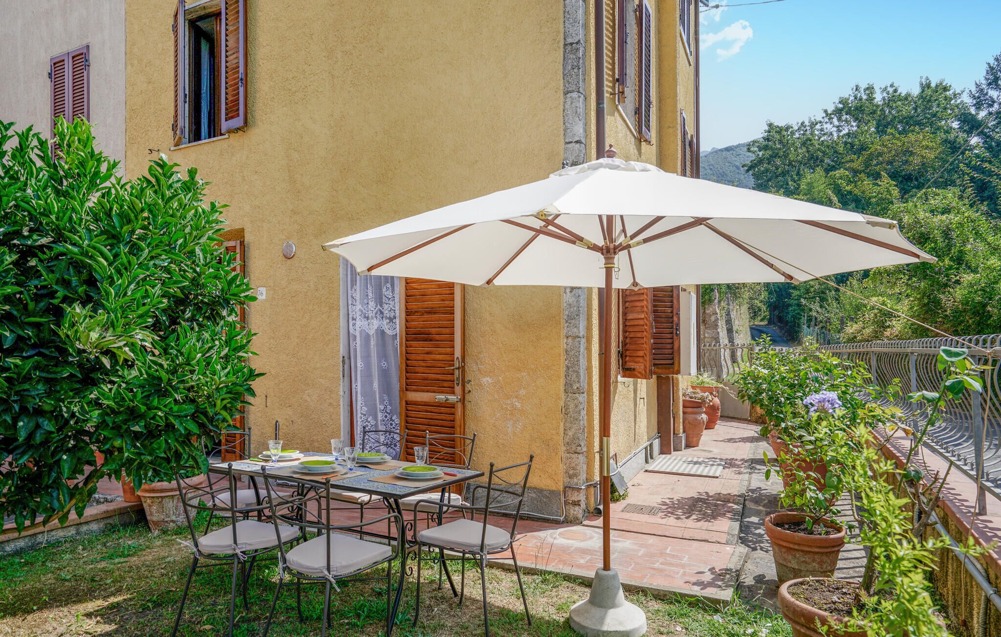 Una terrazza esterna con tavolo e sedie, un ombrellone bianco e piante in vaso.