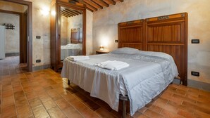 A bedroom with a large bed, wooden headboard, tiled floor, and a door leading to another room.