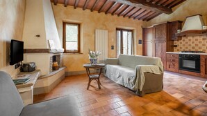A cozy room with a wooden ceiling, a sofa, a small table, a television, and a kitchen area with cabinets and a stove.