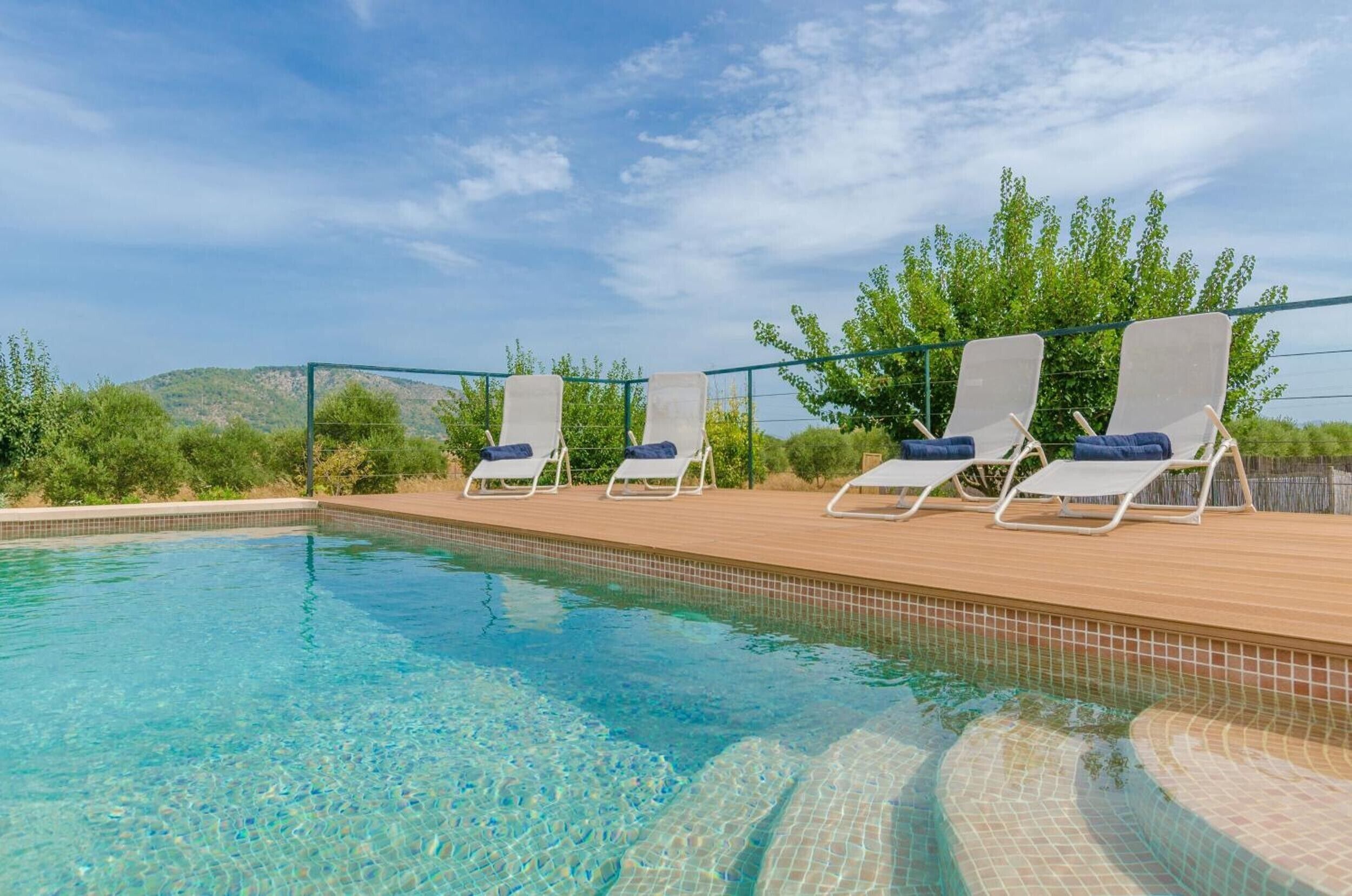 A clear swimming pool with lounge chairs and a view of the landscape.