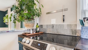 Una cocina con estufa, una planta grande en maceta, un cuchillo colgado y un salpicadero de azulejos.