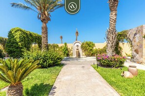 Stroll through lush gardens, lined with palm trees and a stone wall, leading to a beautifully maintained entrance.