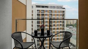 A balcony with a round table and two chairs, overlooking a high-rise building.