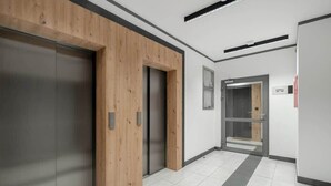A modern hallway with a wooden panel wall, a metallic elevator, and a tiled floor.