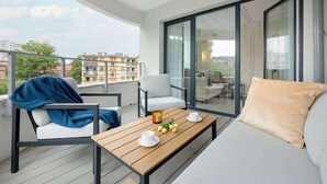 A balcony with a wooden table, two chairs, a sofa, and a glass door leading to an outdoor area.