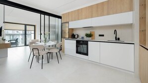 A modern kitchen with white cabinetry, a wooden accent wall, a built-in oven, and a dining area with a round table and chairs.