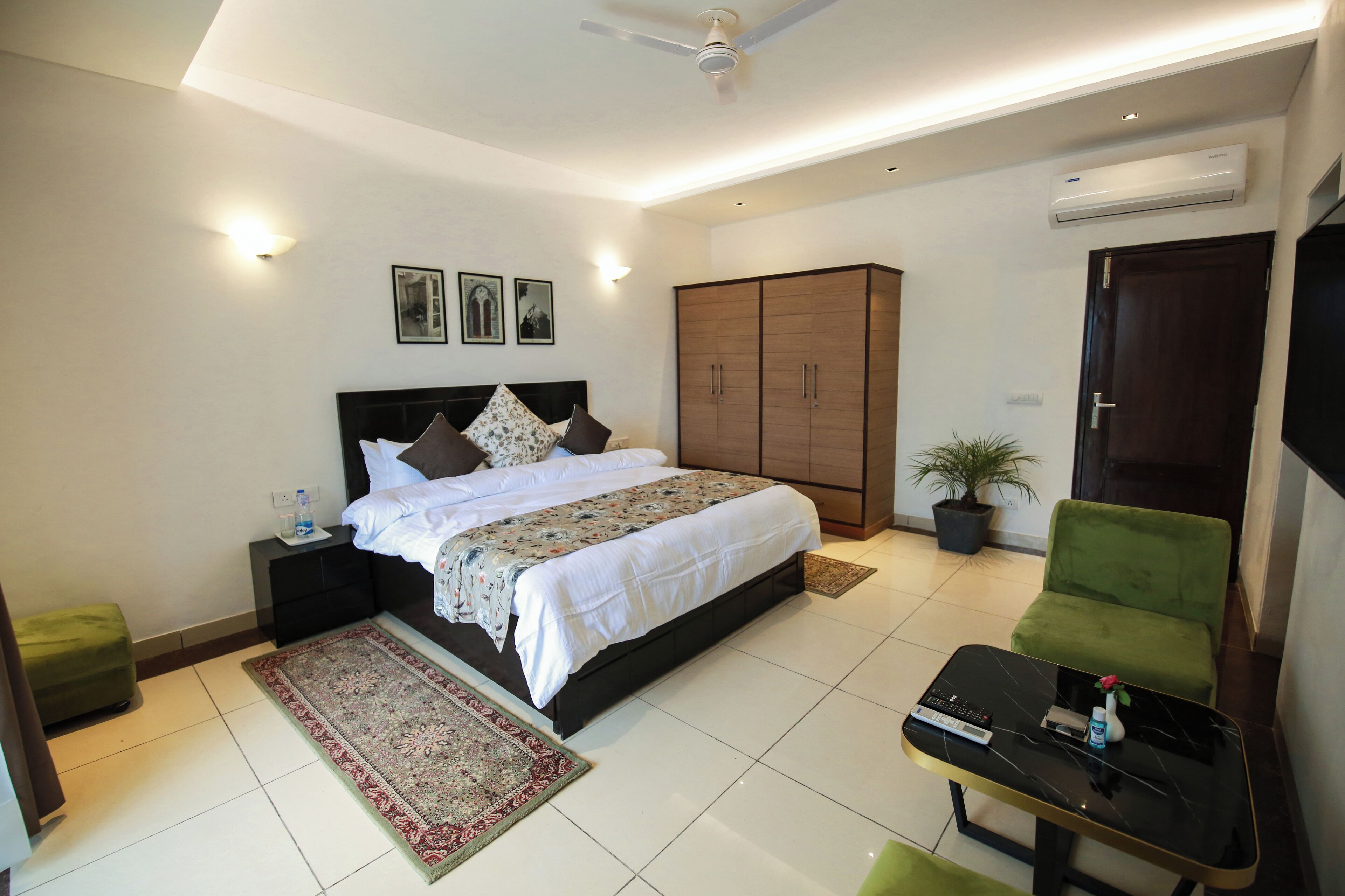 Une chambre à coucher comprenant un lit, une table de chevet, un fauteuil vert, une petite table, une grande armoire et un appareil de climatisation.