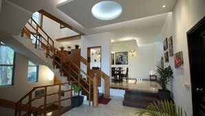 A spacious interior with a wooden staircase, a dining area, and a living space with a large window and ceiling light.