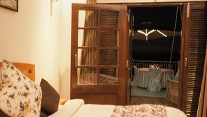 A bedroom with a bed, a wooden door leading to a balcony, and a table set for dining.