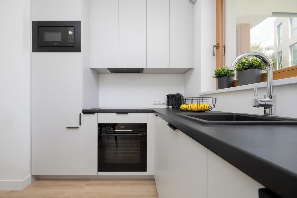 A modern kitchen with white cabinets, a built-in microwave, a black oven, and a black countertop.