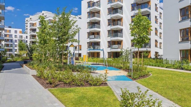 Un immeuble d’appartements moderne composé de plusieurs bâtiments, avec une cour intérieure agrémentée d’une balançoire et une petite piscine.
