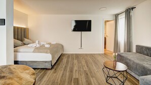 Una camera d'albergo moderna con un letto, un divano, una TV e un piccolo tavolo.