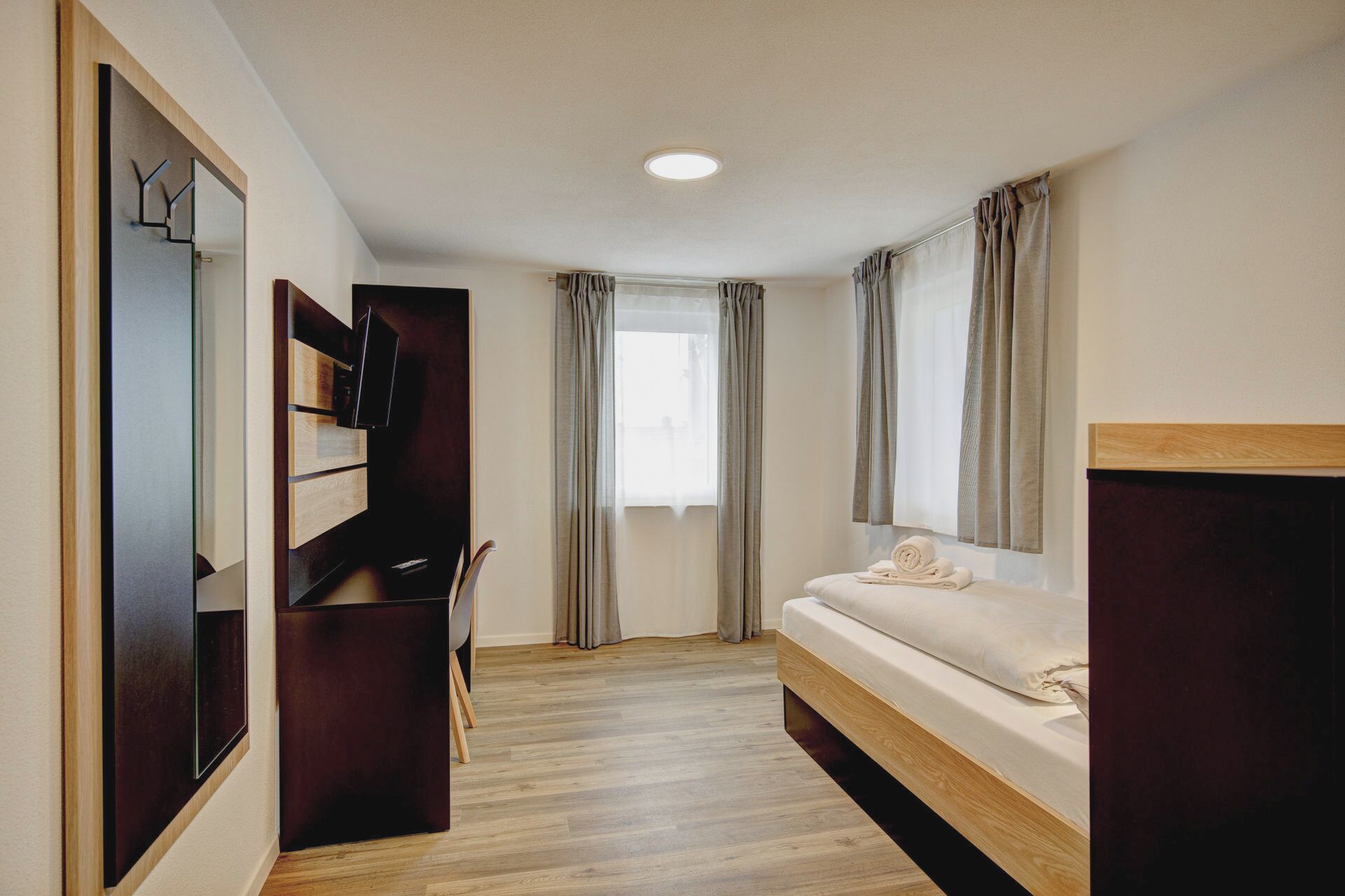 A hotel room with a bed, a desk, a chair, and a TV.
