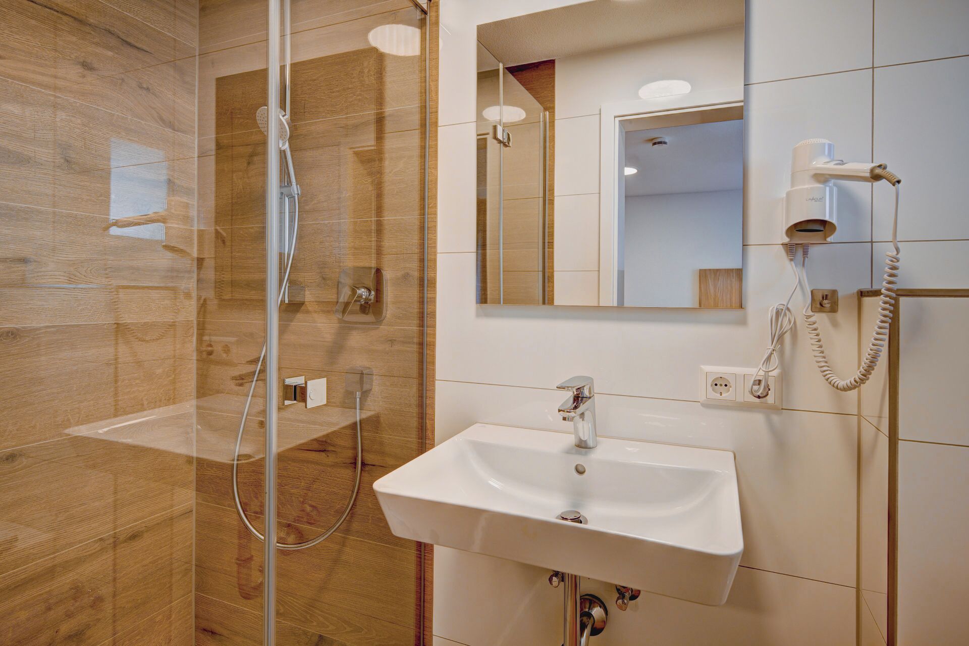 Un baño moderno con cabina de ducha de vidrio, un lavabo blanco y un espejo sobre él.