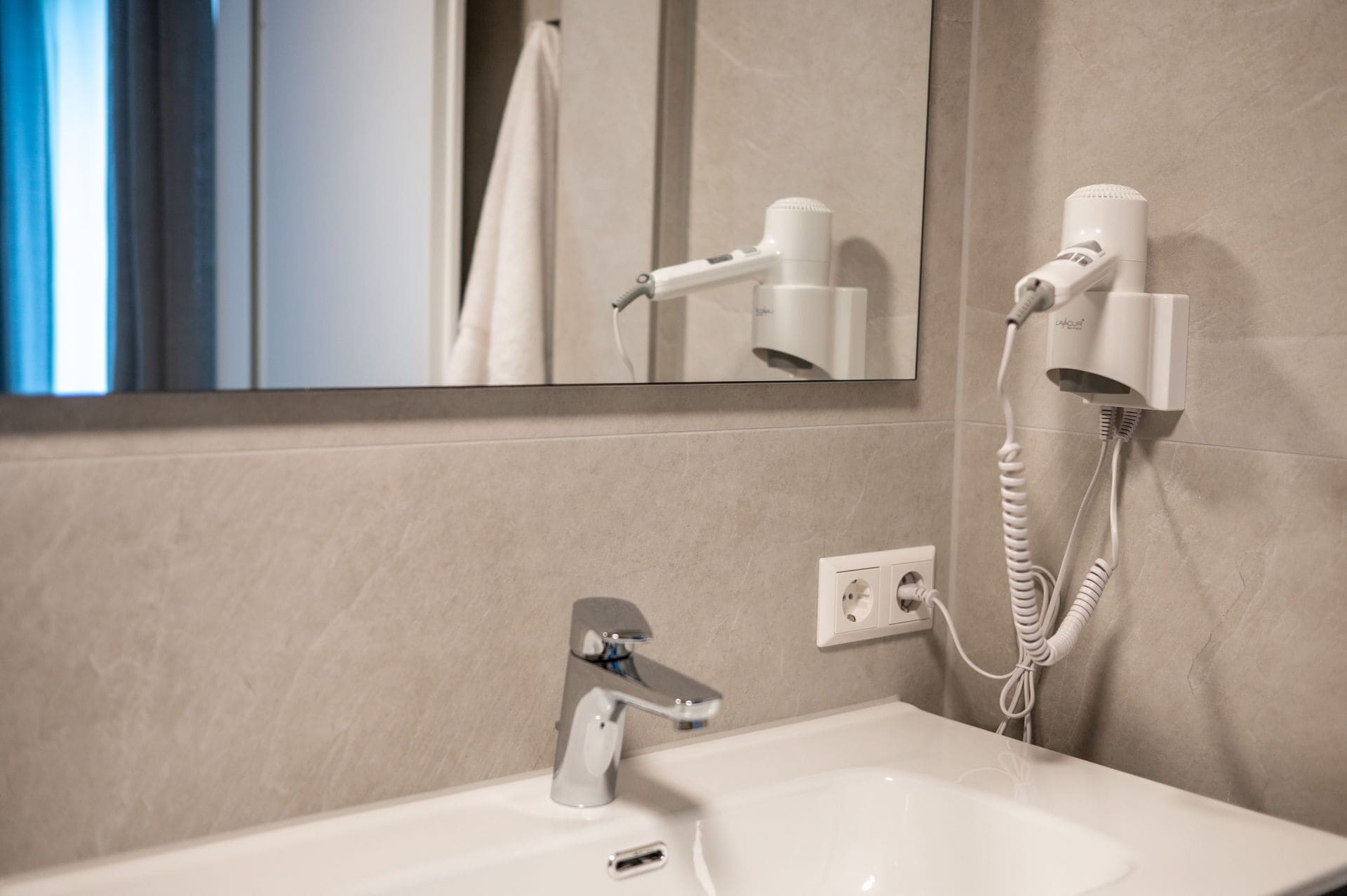 A bathroom with a sink, a mirror, a hairdryer, and a towel rack.