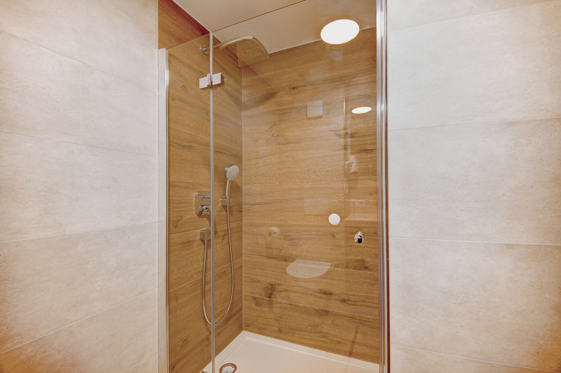 Une douche fermée par des parois en verre, avec un revêtement mural en bois, une douchette à main et un panneau de commande fixé au mur.