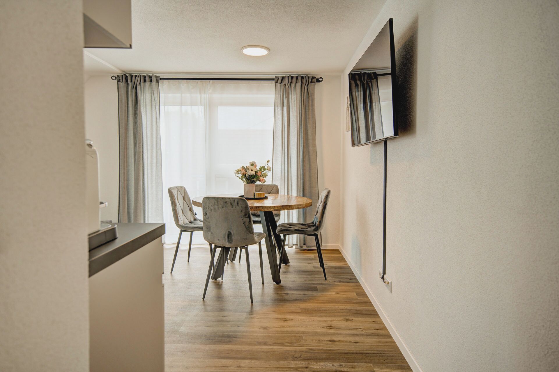 A dining area with a wooden table, four chairs, and a vase of flowers.