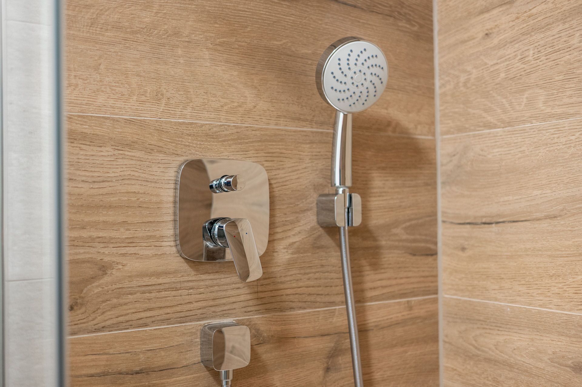 Una ducha con cabezal de ducha de mano y panel de control en la pared.