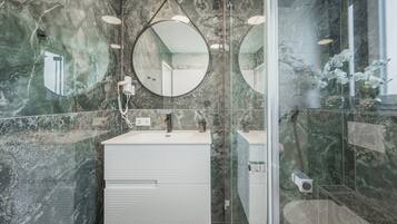 A modern bathroom with a marble wall, a round mirror, a white vanity, and a glass shower enclosure.