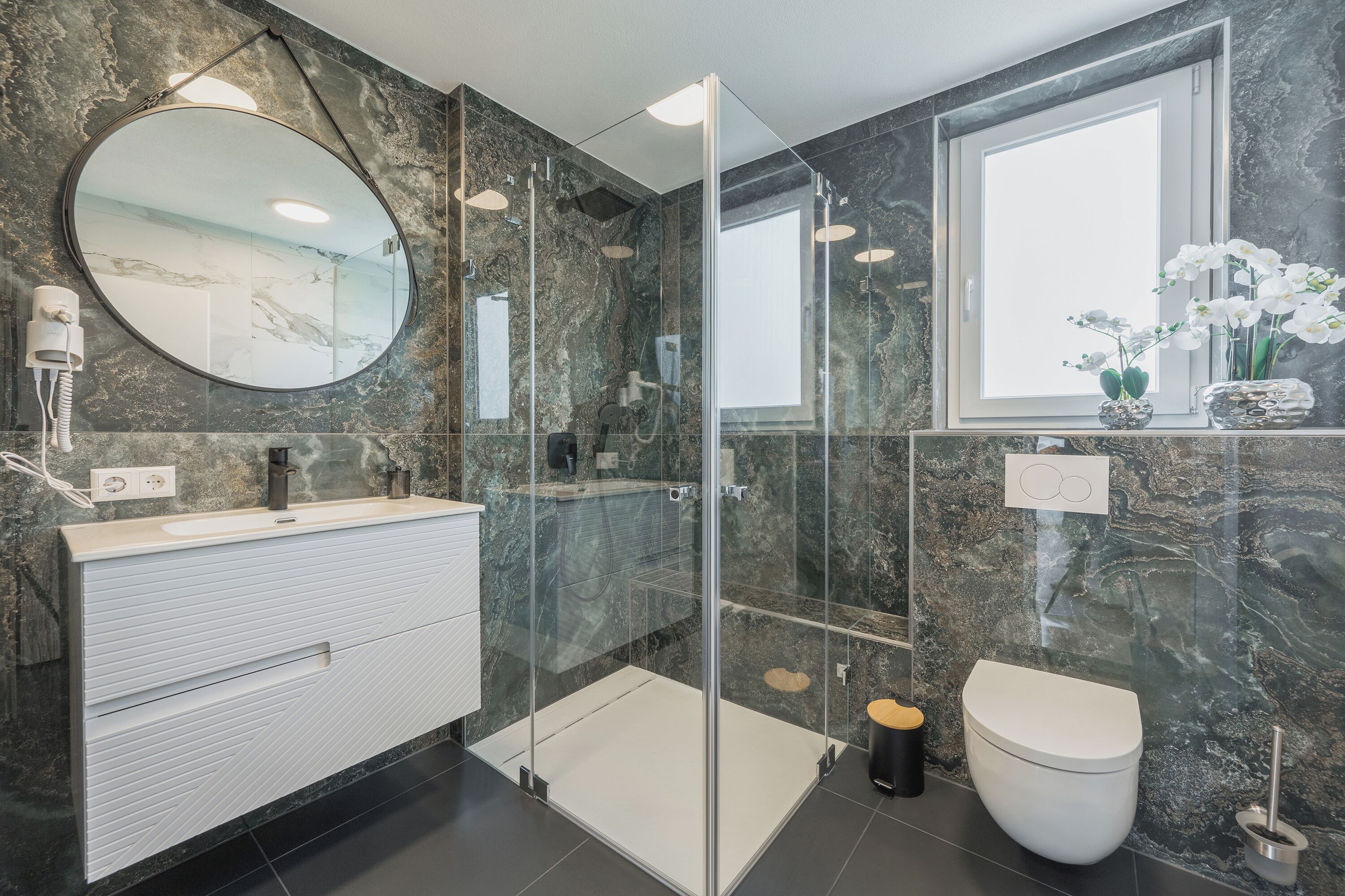 Een moderne badkamer met een douchecabine van glas, een witte wastafel en een toilet.