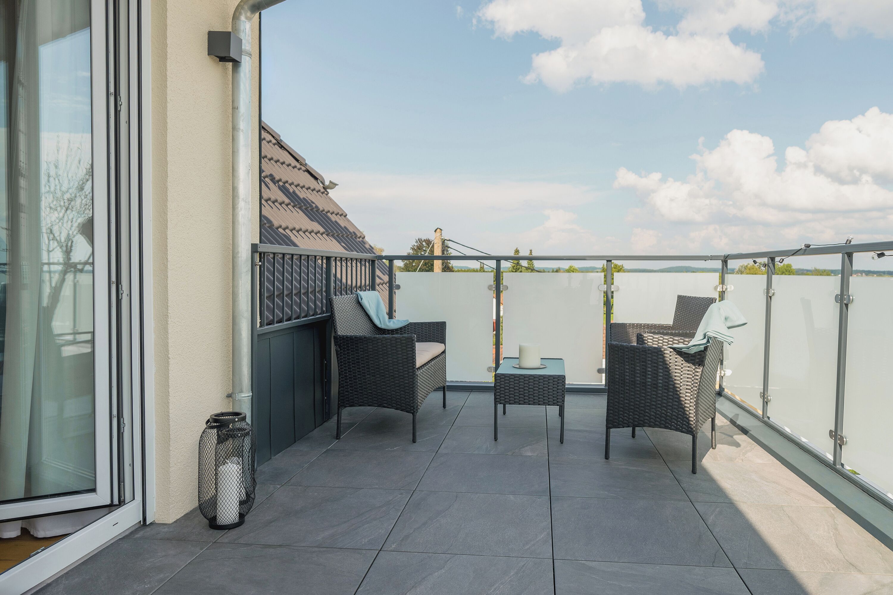 En balkon med to fletstole, et lille bord, en glasdør og havudsigt.