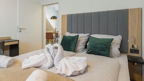 Una camera d'hotel con un letto, due cuscini verdi, una testiera in legno, un comodino, una lampada e una porta che dà su un'altra stanza.