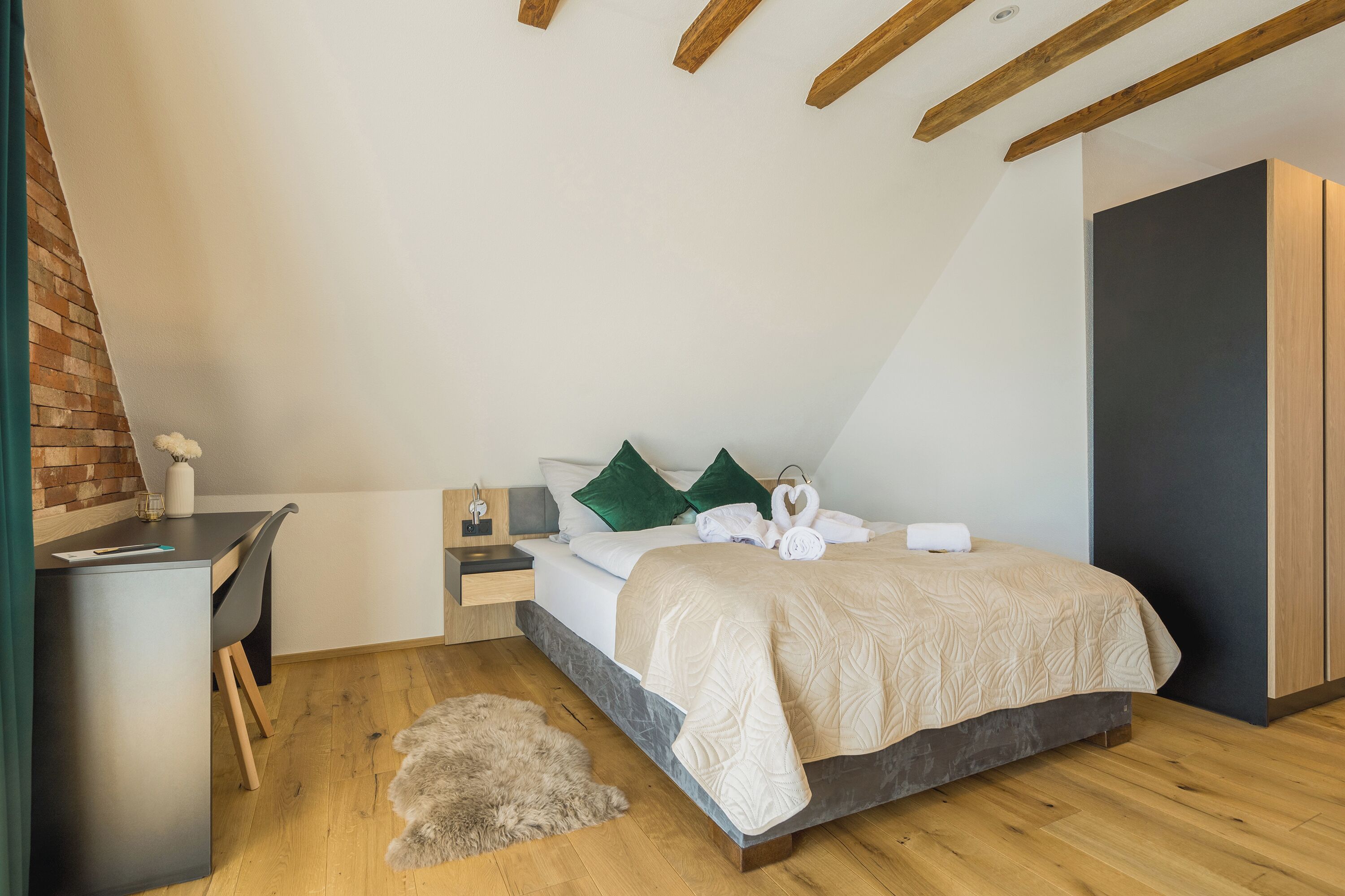 A modern bedroom with a bed, bedside tables, a desk, and a brick wall.