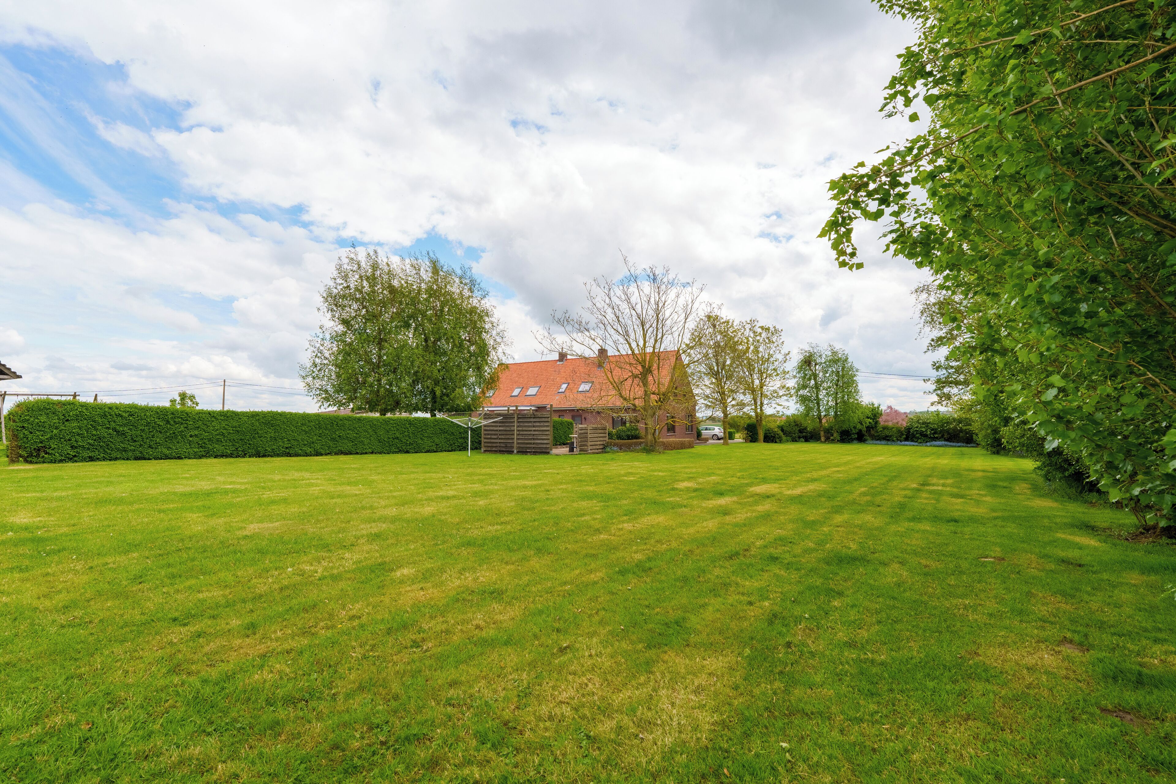 A well-maintained lawn with a red-roofed building in the background, surrounded by trees and a hedge.
