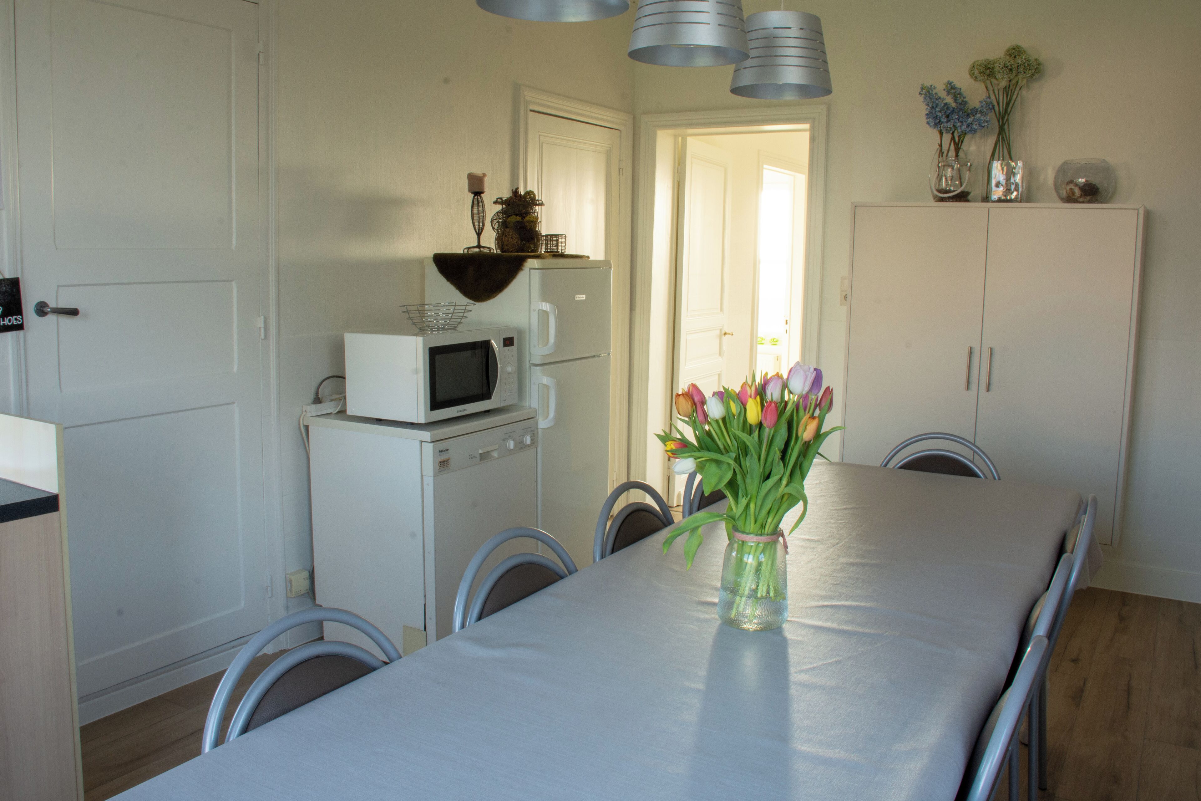 A dining area with a table set for four, a microwave, a refrigerator, and a cabinet with decorative items.