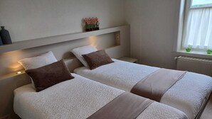 Ein Hotelzimmer mit zwei Betten, einem Nachttisch, einem Regal mit Dekoration und einem Fenster mit Vorhängen.