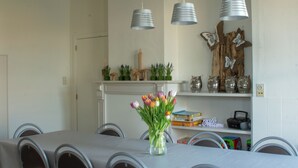 Ein Essbereich mit einem langen Tisch, Stühlen, Pendelleuchten und einem Blumenstrauß.
