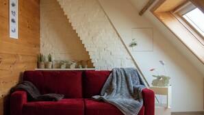 Ein rotes Sofa in einem Raum mit weißer Backsteinwand, Holzboden und einem Oberlicht.