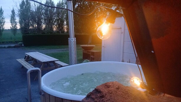 Ein Whirlpool mit einer hölzernen Sitzbank und einem Tisch in der Nähe, umgeben von einem Garten und einer Gartenhütte.