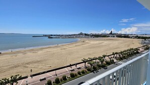 Une plage avec une promenade dallée, des bancs et une vue sur la mer et les bâtiments situés au loin.