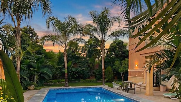 Une piscine dotée d’une terrasse carrelée, entourée de palmiers et de verdure.